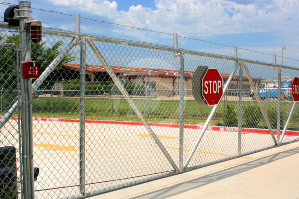 Cantilever access controls gate with chain link and barbed wire along the top of gate for access to a business