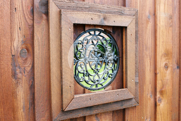 Stained cedar board on board fence with circular decorative ornamental iron fitting