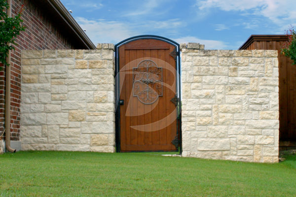 Rounded cedar backyard door with white stone walls and decorative iron fittings.